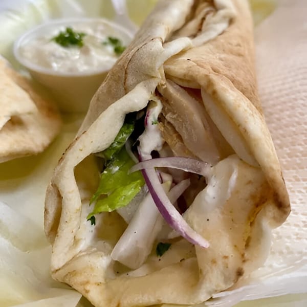 A Mediterranean chicken shawarma wrap with lettuce, onions, and white sauce, served with a side of dip.
