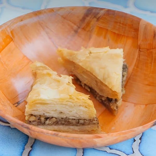 Two triangular pieces of baklava with flaky pastry and nut filling in an orange bowl.