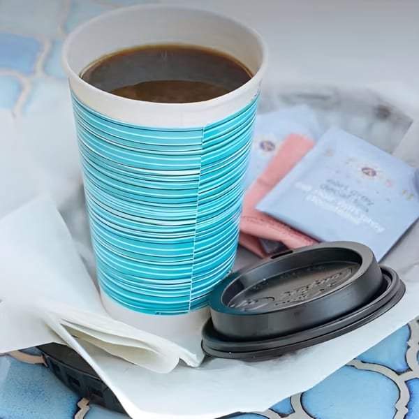 A Bluzone Cafe coffee cup with a blue striped design, lid, and sugar packets on a patterned table.