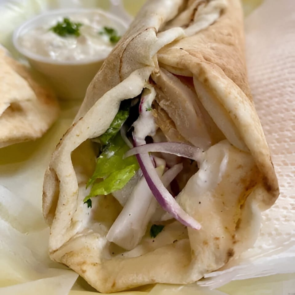 A Bluzone Cafe Mediterranean chicken shawarma wrap with lettuce, onions, and white sauce.