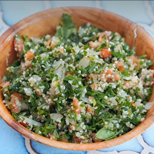 Close-up of a wooden bowl filled with fresh Bluzone Cafe tabbouleh salad, featuring parsley, tomatoes, and bulgur.
