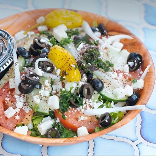 A vibrant Mediterranean salad with olives, feta, tomatoes, and peppers in a wooden bowl.
